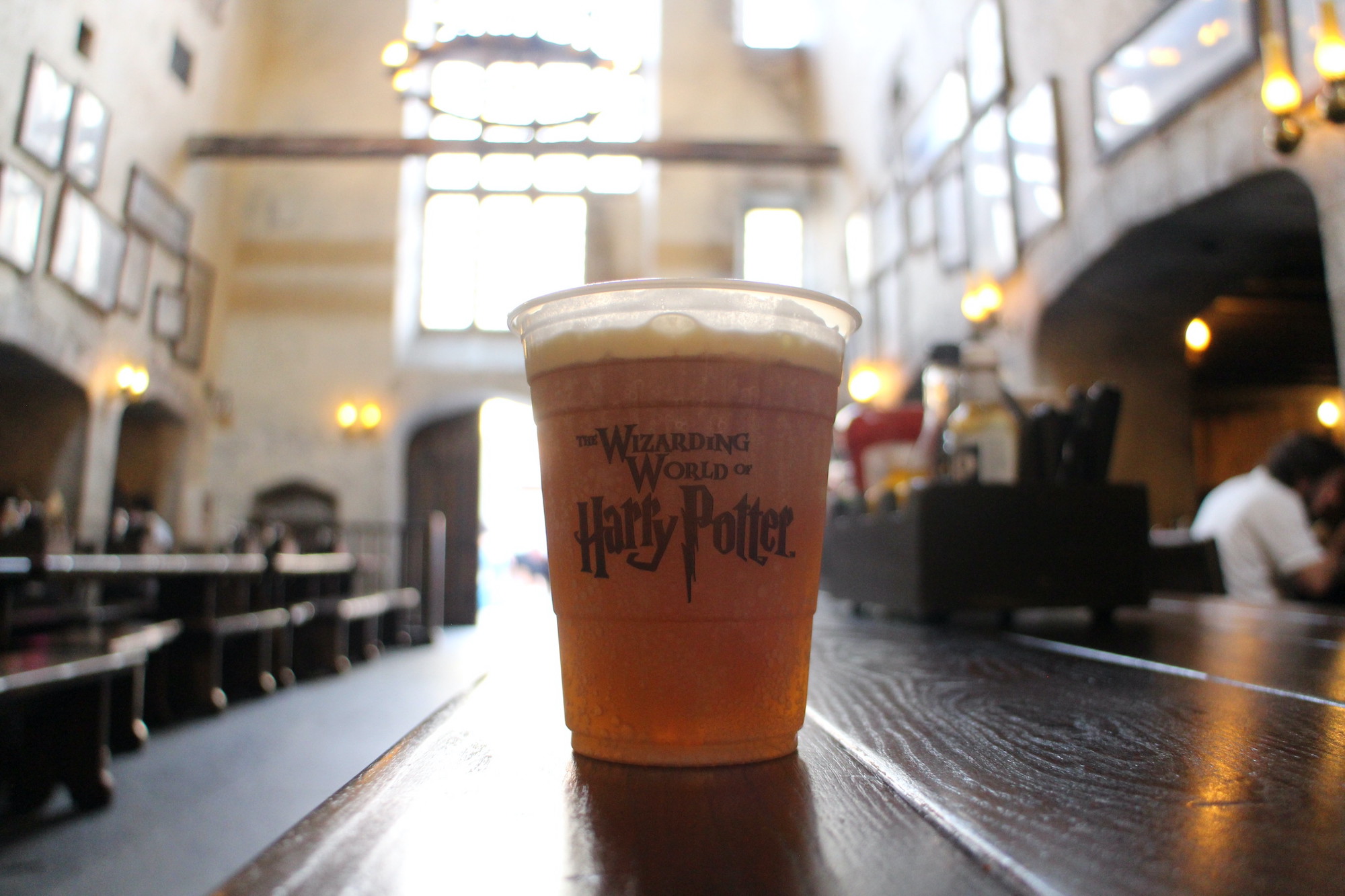 This butterbeer sits on a dark table in The Leaky Cauldron table restaurant, backlit by tall windows and is more accessible with Orlando deals