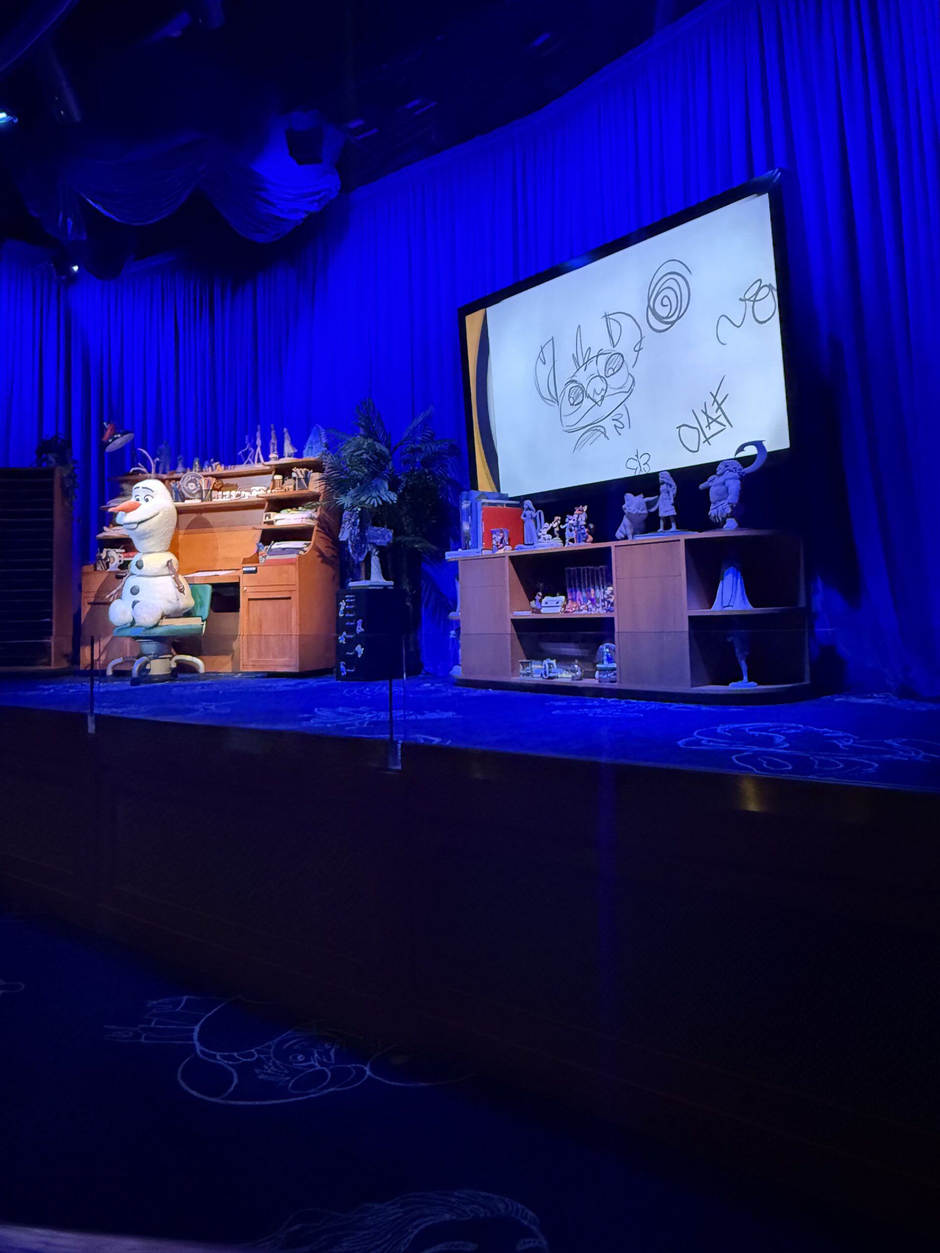 The Disney drawing class room with Olaf working at a desk on stage and his drawing of Stitch displayed on the monitor next to him.