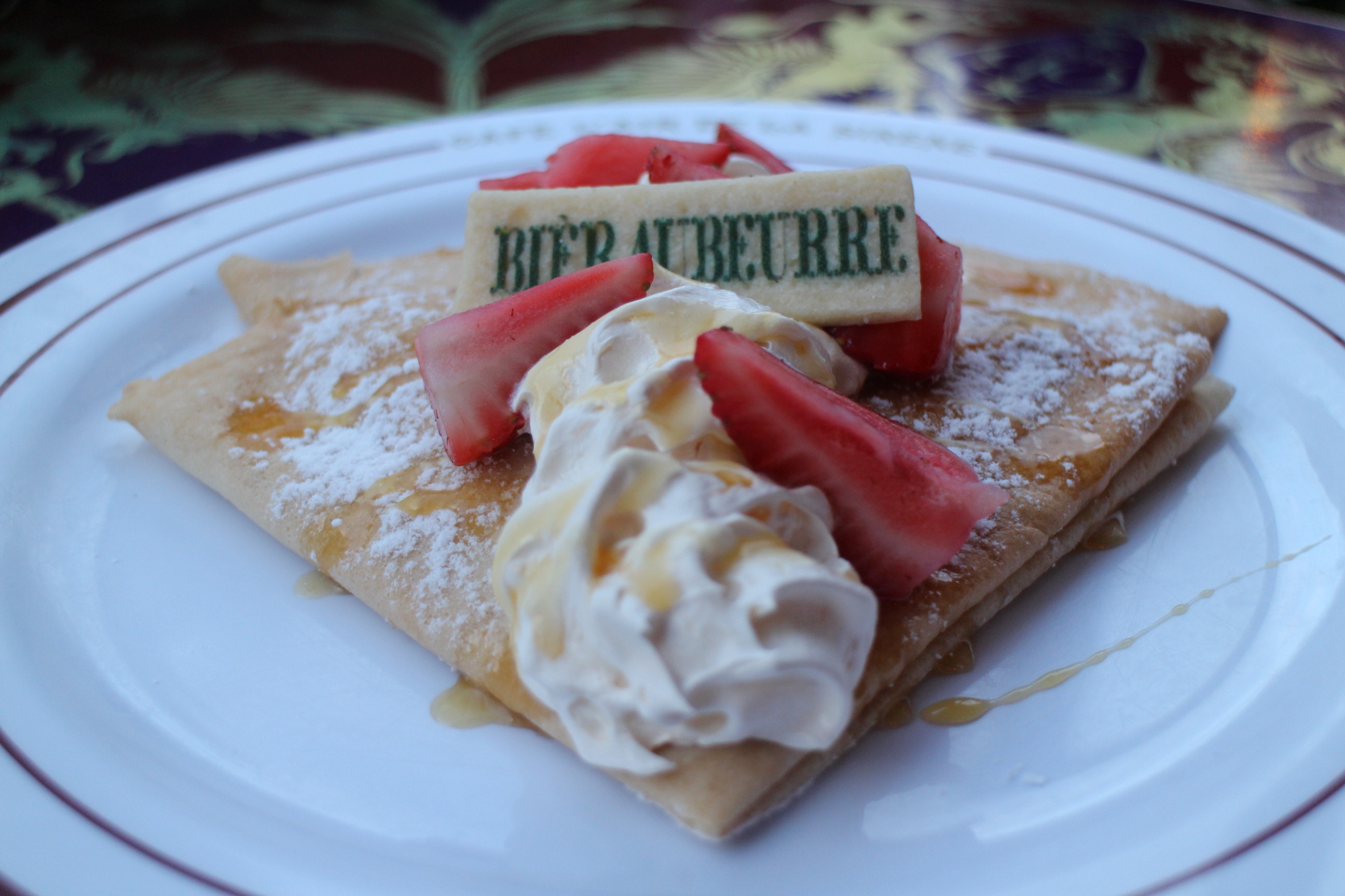 A butterbeer crepe on a white plate topped with strawberries, a shortbread cookie that says bièraubeurre and strawberries.
